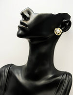 Mannequin head wearing a gold earring with a pearl-like center on a white background