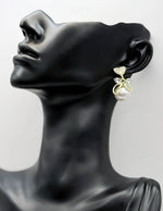 Gold and pearl earring on a black mannequin head against a white background
