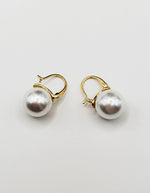 Biya Accessoires gold huggie hoop earrings with large white pearl drop.