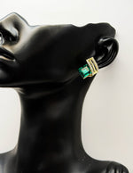 Gold and emerald green earring on a black mannequin bust.