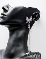 Close up of imitation jewelry uae statement earrings featuring purple rhinestone wings and pearls.