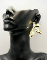 Gold leaf earring on a black mannequin bust against a white background