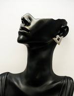 Black mannequin head with a diamond-shaped earring on a white background