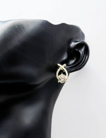 Gold earring with a diamond on a black mannequin ear against a white background