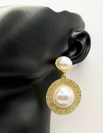Pearl earrings with gold accents on a black mannequin ear.