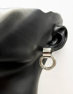 Silver earring on a black ear model with a white background