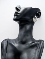 Black mannequin head wearing a sparkling silver earring against a white background