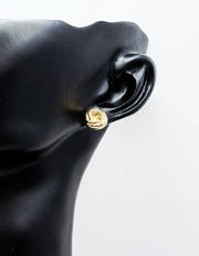 Gold earring on a black mannequin ear against a white background