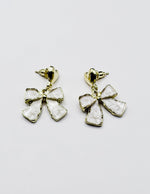 Biya Accessoires gold heart and cream enamel bow drop earrings.