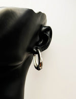 Silver hoop earring on a black mannequin ear against a white background