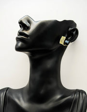 Black mannequin head wearing gold hoop earrings on a white background
