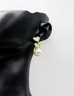Close up of elegant imitation jewelry uae featuring a pavé crystal heart, gold bow, and faux pearl drop.
