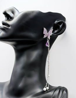 Close up of imitation jewelry uae statement earrings featuring purple rhinestone wings and pearls.