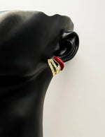 Close up of imitation jewelry uae statement studs featuring red enamel and pavé clear stones.
