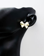 Gold bow-shaped earring on a black mannequin ear against a white background