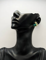 Black mannequin head wearing gold and green earrings against a white background