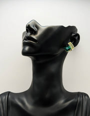 Black mannequin head wearing gold and green earrings against a white background