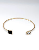 Gold bracelet with black and clear gemstones on a white background
