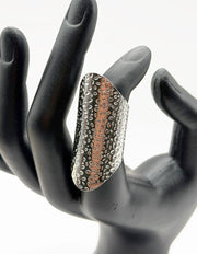 Decorative ring with textured design on a black mannequin hand against a white background