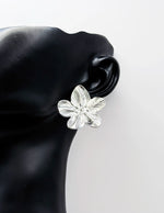 Silver flower-shaped earring on a black mannequin ear against a white background