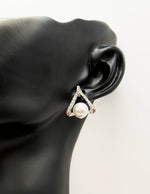 Pearl earring on a black mannequin ear with a white background